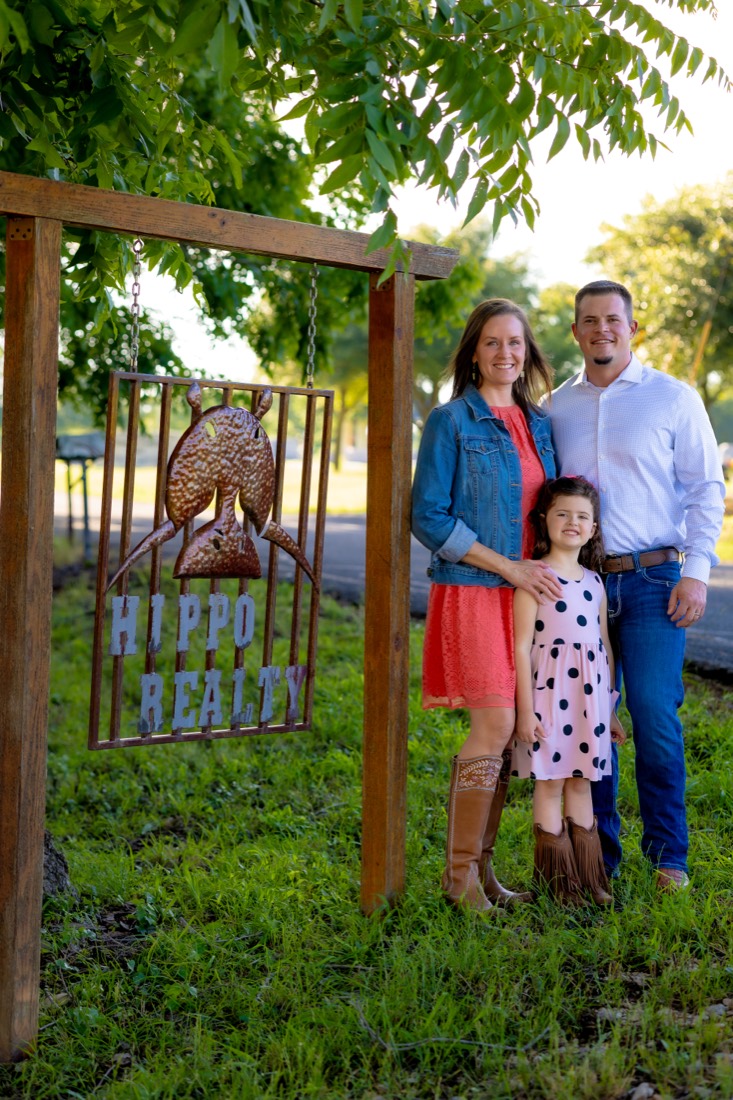 Brooke and Russell Daniel with their daughter beside the hand-forged Hippo Realty sign in Hutto
